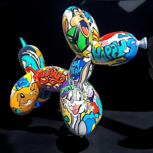 Pode incluir: Uma escultura de cão de balão com uma pintura vibrante em estilo graffiti, apresentando vários personagens de desenhos animados, incluindo Bugs Bunny e Scooby-Doo. A superfície está coberta com ilustrações coloridas e textos como "Happy" e "Oh Yeah".