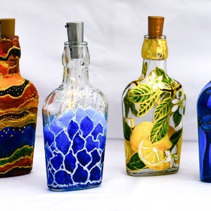 Könnte beinhalten: Sechs handbemalte Glasflaschen mit Korkstopfen. Die Flaschen sind mit verschiedenen Designs verziert, darunter Flamingos, ein Heißluftballon, Zitronen und abstrakte Muster. Die Flaschen sind alle in verschiedenen Farben, darunter Blau, Grün, Rot und Gelb.