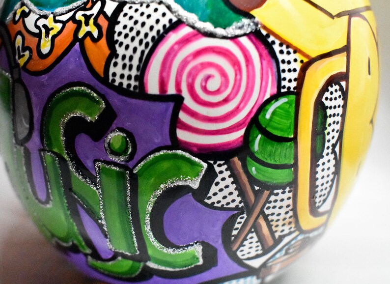 May include: A purple, green, yellow, and white painted ornament with a swirl design, polka dots, and the word "UNIC" in green letters.