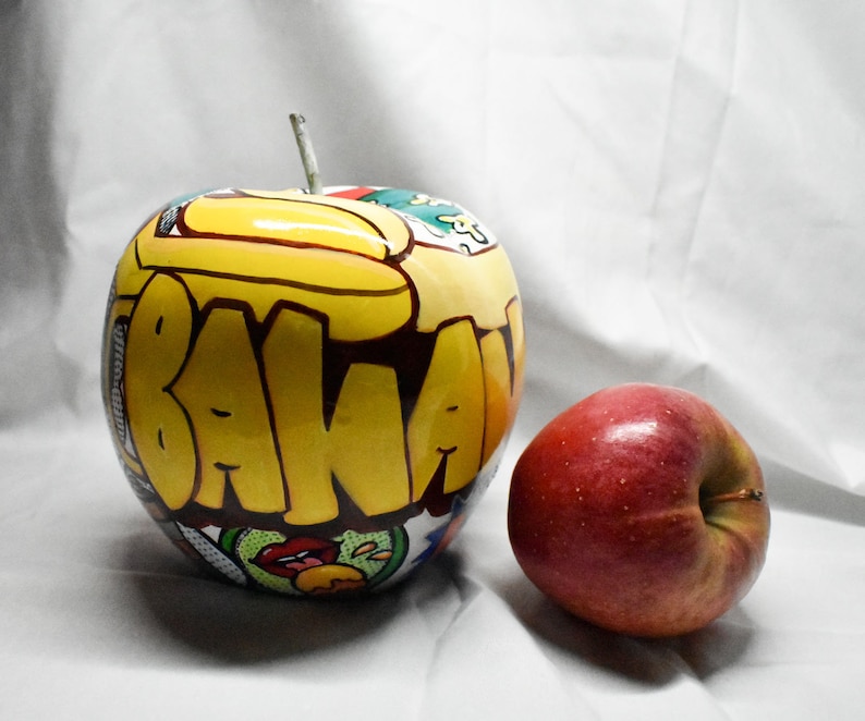 May include: A red apple and a yellow apple with the word "BANANA" painted on it in black and yellow letters.