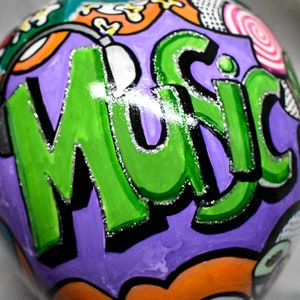 May include: A purple, green, black, and white painted sphere with the word "Music" written in large, bold letters. The sphere has a glossy finish and is decorated with various colorful designs.