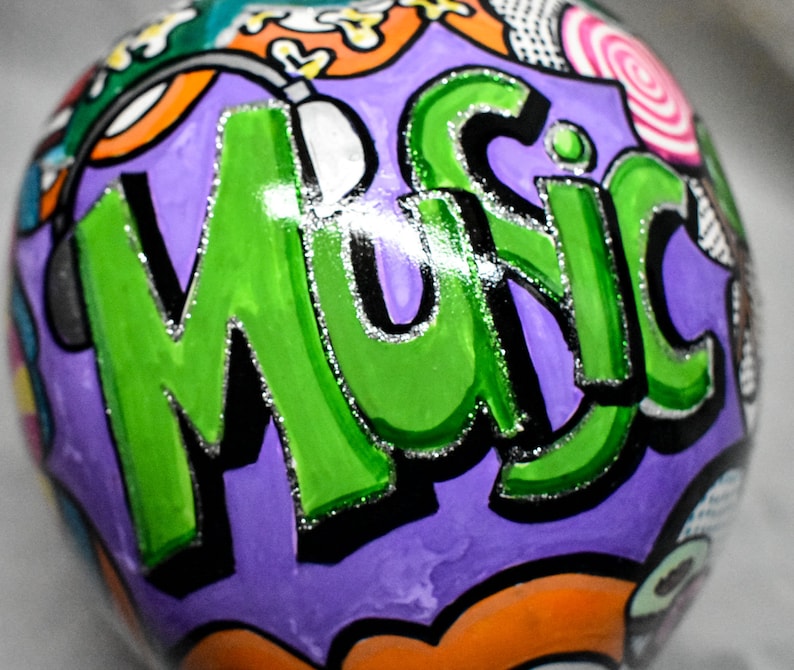 May include: A purple, green, black, and white painted sphere with the word "Music" written in large, bold letters. The sphere has a glossy finish and is decorated with various colorful designs.
