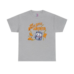 May include: A gray t-shirt with the text "The Brave Little Air Fryer" in orange and yellow letters. A cartoon air fryer with a face and arms is holding french fries.