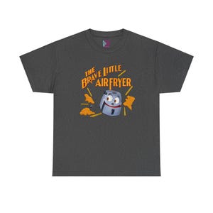 May include: A dark heather grey t-shirt with a cartoon air fryer with googly eyes and a smiling face. The air fryer is surrounded by orange french fries. The text "The Brave Little Air Fryer" is printed in orange and white on the shirt.