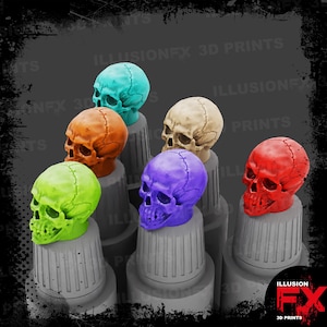 May include: A collection of six miniature human skull replicas in vibrant colours including lime green, orange, turquoise, beige, purple, and red. Each skull is mounted on a grey, cylindrical, ribbed base, displaying detailed cranial sutures.