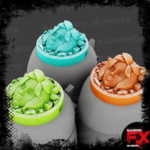 Puede incluir: Tres objetos decorativos circulares impresos en 3D que presentan un rostro humano esculpido rodeado de elementos en forma de hoja. Un objeto es azul cerceta, otro verde lima y otro naranja. Cada pieza está montada sobre una base gris redondeada.