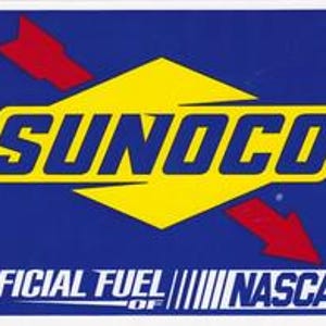 May include: A rectangular sticker with the Sunoco logo, featuring a yellow diamond shape with the word "SUNOCO" in blue letters. Red arrows point towards the center. Below, the text reads "OFFICIAL FUEL OF NASCAR" in white.