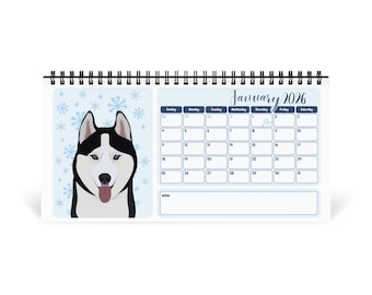 Può includere: Un calendario da scrivania a spirale per gennaio 2026 con un cane husky dei cartoni animati con pelo bianco e nero e occhi blu. Il calendario ha uno sfondo azzurro chiaro con disegni di fiocchi di neve.