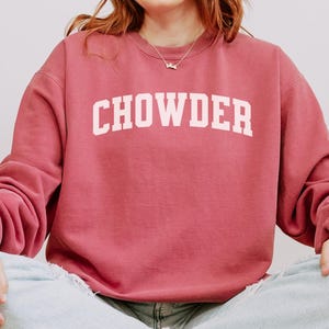 Puede incluir: Sudadera de color carmesí con la palabra "CHOWDER" en letras blancas. La sudadera es de estilo cuello redondo y está hecha de un material suave. La palabra "CRIMSON" se muestra en blanco en la parte inferior de la imagen.