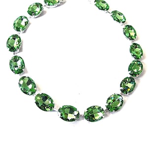 May include: A necklace featuring a series of oval-shaped, faceted green gemstones. The gemstones are set in a silver-toned metal and arranged in a circular pattern. The necklace is displayed against a white background, highlighting the vibrant green color of the stones.