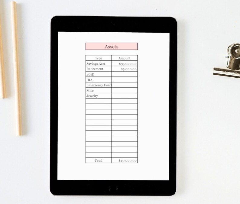 Puede incluir: Una tableta negra muestra una hoja de seguimiento de activos financieros. La hoja est&aacute; organizada en formato de tabla, con columnas para 'Tipo' e 'Importe'. El total de activos es de 36.800 &euro;. La tableta est&aacute; sobre una superficie blanca.