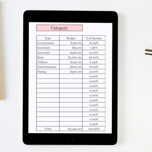K&ouml;nnte beinhalten: Ein schwarzes Tablet zeigt eine Budget-Tabelle mit Kategorien wie Autozahlung, Lebensmittel und Miete. Die Tabelle zeigt Budgetbetr&auml;ge und Einkommensprozents&auml;tze. Eine Metallklammer und Holzst&auml;be befinden sich im Hintergrund.