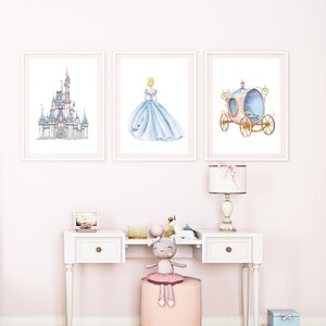 May include: Three framed prints of Cinderella themed artwork. The prints feature a watercolor illustration of Cinderella's castle, Cinderella in her blue ball gown, and Cinderella's carriage.