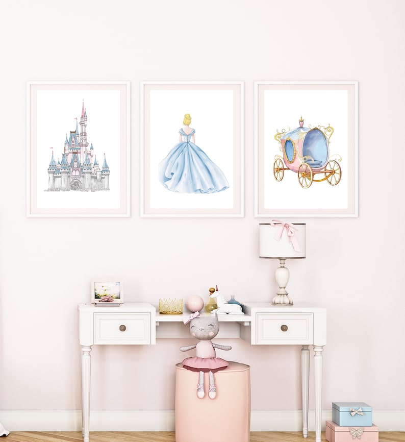 May include: Three framed prints of Cinderella themed artwork. The prints feature a watercolor illustration of Cinderella's castle, Cinderella in her blue ball gown, and Cinderella's carriage.