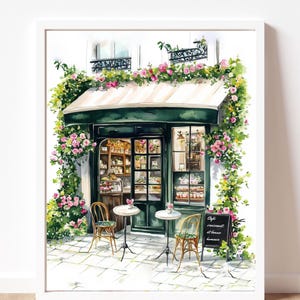 May include: A watercolor painting of a Parisian cafe with a green awning and a chalkboard sign that reads "Cafe, croissant et th&eacute;s, lumi&egrave;re". The cafe is decorated with flowers and has two tables with chairs outside.