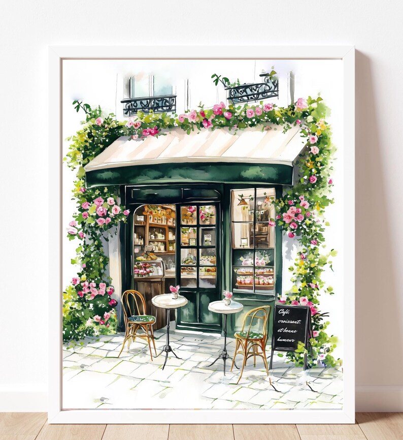 May include: A watercolor painting of a Parisian cafe with a green awning and a chalkboard sign that reads "Cafe, croissant et th&eacute;s, lumi&egrave;re". The cafe is decorated with flowers and has two tables with chairs outside.