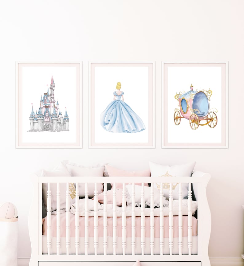 May include: Three framed prints depicting a fairytale theme. The first print shows a detailed illustration of a castle with towers and spires. The second print shows a princess in a blue gown, facing away from the viewer. The third print shows a pink carriage with gold accents and wheels.