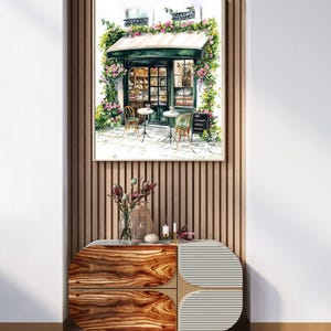 May include: A watercolor painting of a Parisian cafe with a green awning, flowers, and two tables with chairs. The cafe is surrounded by a white building with a window and a sign that reads "Cafe", "Gourmandises", and "Ap&eacute;ros".