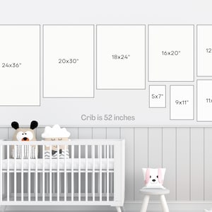 May include: A white crib with a white mattress and two stuffed animals on top. The crib is 52 inches wide. There are nine framed pictures on the wall above the crib, with measurements in inches.