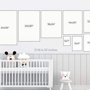 May include: A white crib with a white mattress and two stuffed animals on top. The crib is 52 inches wide. There are nine framed pictures on the wall above the crib, with measurements in inches.