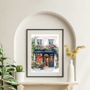 May include: A watercolor painting of a storefront with a black awning and a sign that reads "Le Jardin." The storefront is decorated with flowers and plants. The building is white with black window frames.