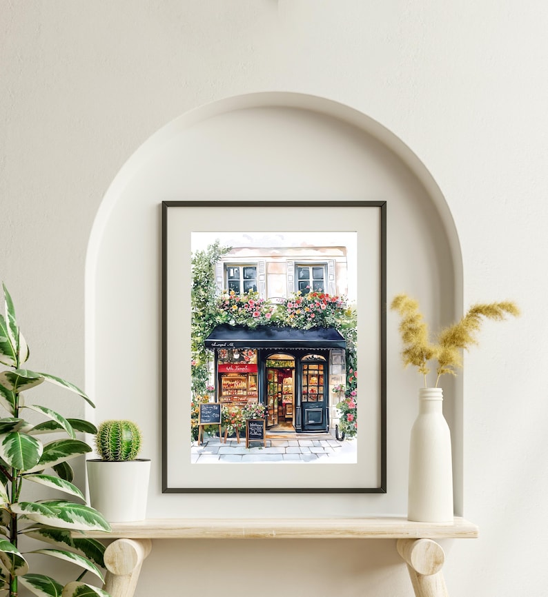 May include: A watercolor painting of a storefront with a black awning and a sign that reads "Le Jardin." The storefront is decorated with flowers and plants. The building is white with black window frames.