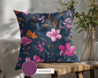 May include: A square throw pillow featuring a dark navy blue background with a floral pattern of pink, magenta, and orange blossoms and brown leaves. A circular inset shows the reverse side with a vertical dark purple and black striped pattern.