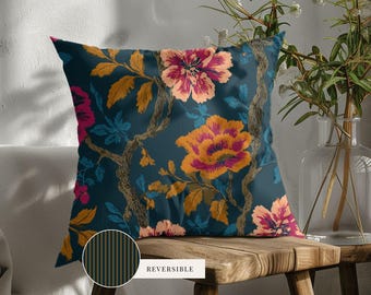 May include: A square throw pillow featuring a dark teal background with a vibrant floral pattern of orange, pink, and yellow flowers and brown branches. A circular inset shows the reverse side, which has thin vertical black and gold stripes.
