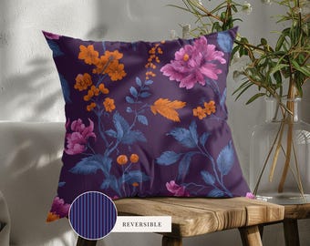 May include: A square throw pillow featuring a dark purple background with a floral pattern of orange and pink blossoms and blue leaves. A circular inset shows the reverse side of the pillow, which has a dark purple and blue vertical striped pattern.