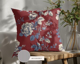 May include: A square throw pillow featuring a deep red background with a repeating pattern of light blue and white floral blossoms and leaves. A small circular inset shows the reverse side, which has a blue and white vertical striped pattern.