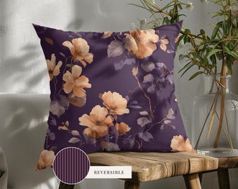 May include: A square throw pillow featuring a dark purple background with a pattern of light orange flowers and muted purple leaves. A circular inset shows the reverse side of the pillow, which has a dark purple and light purple vertical stripe pattern.
