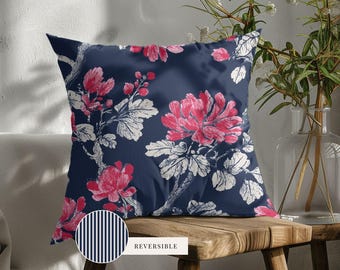 May include: A square throw pillow featuring a dark navy blue background with a repeating pattern of pink flowers and white leaves. A circular inset shows the reverse side of the pillow, which has a pattern of thin vertical navy and white stripes.