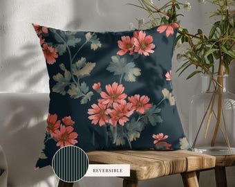May include: A square throw pillow featuring a dark navy blue background with a repeating pattern of coral pink flowers and muted green foliage. A small circular inset shows the reverse side, which has a dark navy blue and thin vertical stripe pattern.