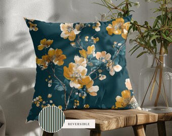 May include: A square throw pillow featuring a dark teal background with a yellow floral pattern. A circular inset shows the reverse side of the pillow, which has a dark teal and white vertical striped pattern with the text REVERSIBLE printed nearby.