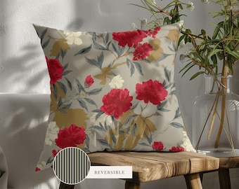 May include: A square throw pillow featuring a floral pattern with vibrant red peonies, muted green leaves, and gold accents on a light beige background. A circular inset shows the reverse side, which has a black and white vertical stripe pattern.