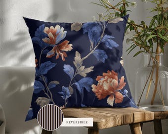 May include: A square throw pillow featuring a dark navy blue background with a floral pattern of orange and light blue blossoms and leaves. A circular inset shows the reverse side of the pillow, which has a pattern of thin vertical black stripes.