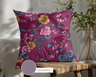 May include: A square throw pillow featuring a deep magenta background with a floral pattern of yellow and pink blossoms, green leaves, and thin stems. A circular inset shows the reverse side with a pattern of thin vertical black and pink stripes.