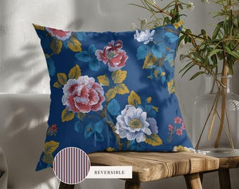 May include: A square throw pillow featuring a deep blue background with a floral pattern of pink, white, and yellow flowers and leaves. A small circular inset shows the reverse side of the pillow, which has a brown and white vertical stripe pattern.
