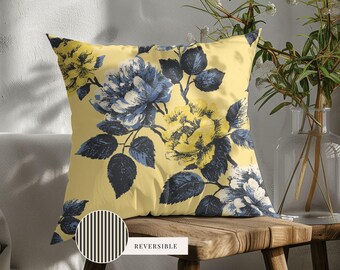 May include: A square throw pillow featuring a yellow background with a dark blue and yellow floral pattern. A circular inset shows the reverse side of the pillow, which has a black and white vertical stripe pattern. The word REVERSIBLE is printed.
