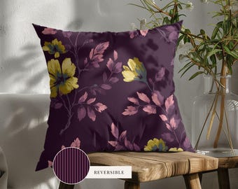May include: A square throw pillow featuring a dark purple background with a floral pattern of yellow blossoms and pinkish-purple leaves. A circular inset shows the reverse side of the pillow, which has a dark purple and black vertical striped pattern.