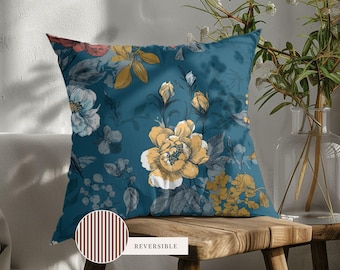 May include: A square throw pillow featuring a dark teal background with a floral pattern of yellow, white, and muted red blossoms and leaves. A circular inset shows the reverse side of the pillow, which has a brown and white vertical stripe pattern.