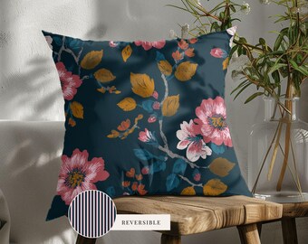 May include: A square throw pillow featuring a dark teal background with a floral pattern of pink blossoms and mustard yellow leaves. A circular inset shows the reverse side, which has a pattern of thin vertical black and white stripes.