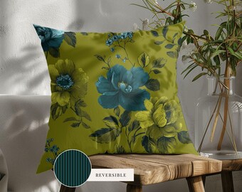 May include: A square throw pillow featuring a dark olive green background with a floral pattern of large teal and yellow-green flowers and leaves. A small circular inset shows the reverse side with a dark teal and black vertical striped pattern.
