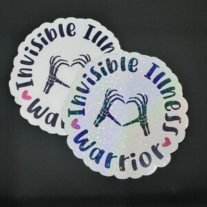 May include: Two round white stickers with a black skeleton hand making a heart shape. The text on the stickers reads "Invisible Illness Warrior" with a pink heart on each side of the text.