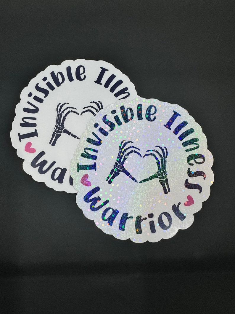 May include: Two round white stickers with a black skeleton hand making a heart shape. The text on the stickers reads "Invisible Illness Warrior" with a pink heart on each side of the text.