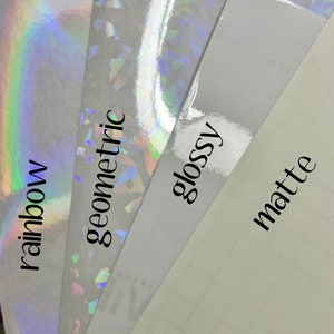May include: Four samples of vinyl adhesive paper with different finishes: rainbow iridescent, geometric iridescent, glossy, and matte. The text labels are "rainbow", "geometric", "glossy", and "matte".