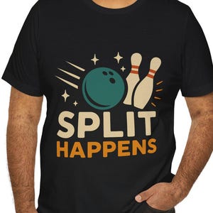 Può includere: T-shirt nero con grafica a tema bowling. Il design presenta una palla da bowling turchese, due birilli e le parole "SPLIT HAPPENS" in arancione e bianco. Un capo d'abbigliamento casual.