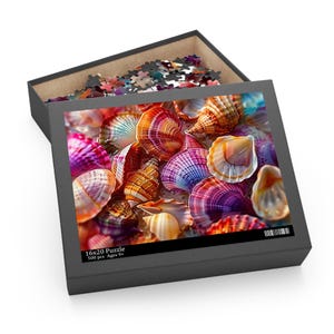 Puede incluir: Una caja de rompecabezas con un diseño de conchas marinas coloridas. La caja está abierta, revelando las piezas del rompecabezas y la imagen completa de varias conchas en tonos naranja, morado y blanco. El texto "16x20 Puzzle 500 pcs Ages 9+" también es visible.