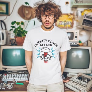 Op de afbeelding: Wit T-shirt met een afbeelding van een toets van een toetsenbord met de tekst "Clickity Clack Attack" erop gedrukt.