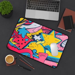 May include: A colorful, abstract design mousepad with a white computer mouse on top. The design features bright pink, yellow, blue, and red colors with a graffiti-style pattern.
